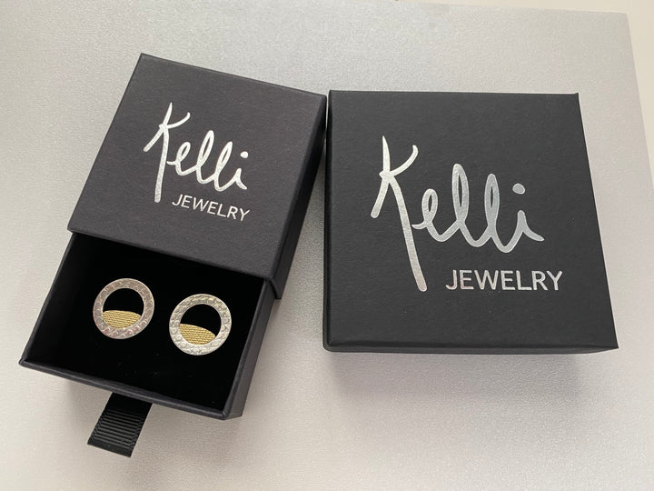 Kelli Jewelry two black jewelry boxes with Kelli Jewelry Logo-Circling Back Disc Silver and 14kt yellow gold stud earrings. Earrings have textured patterns and three quarter inches diameter-Kelli Montgomery Jewelry